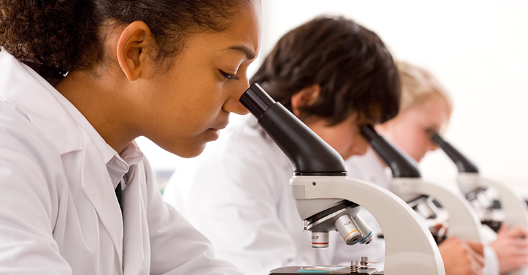 Photo of children in lab coats looking intently into microscopes.